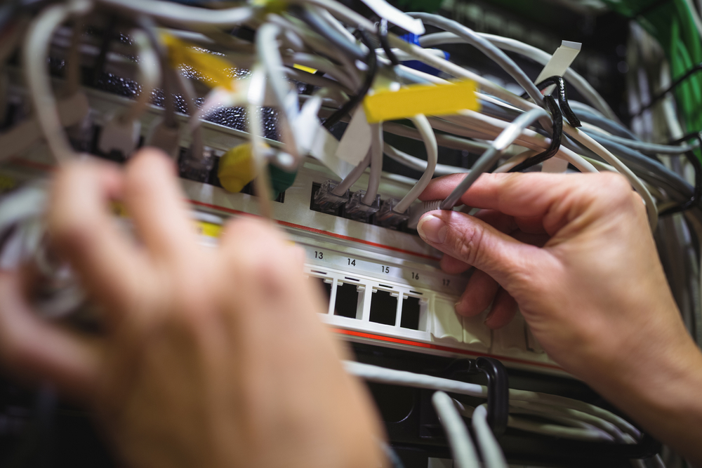 Technician plugging patch cable in a rack mounted server in server room