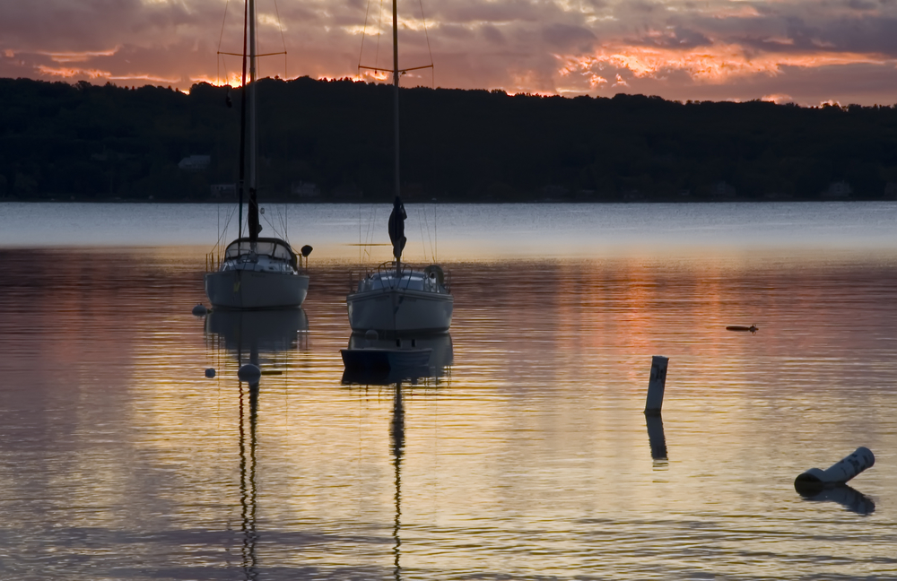 Two sailboats at anchor near shore at dawn